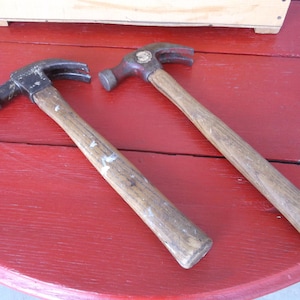 May include: Two wooden-handled hammers with metal heads. One hammer has a black head and the other has a red head.
