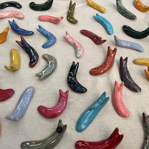 May include: A collection of colorful ceramic chopsticks in various shapes and designs. The chopsticks are made of glazed ceramic and feature a variety of colors, including blue, green, red, yellow, and black.