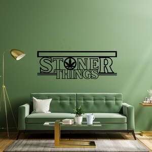 May include: A green wall with a black and white vinyl decal that says "Stoner Things" with a marijuana leaf in the middle of the word "Stoner". A green sofa with a white cushion is in front of the wall.
