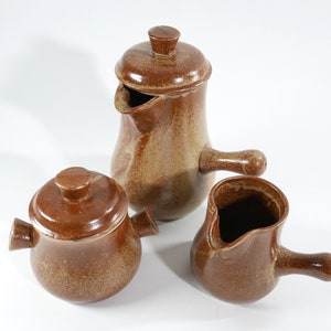 Peut inclure: Un ensemble de trois pièces de cuisine en céramique brune avec un glaçage moucheté. L'ensemble comprend un pot à crème, un sucrier avec un couvercle et un pichet.