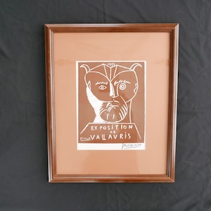 May include: A framed print of a black and white line drawing of a man's face with the text "EXPOSITION DE VALLAURIS" and "Picasso" in white lettering on a brown background.