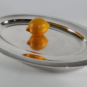 May include: A silver oval serving tray with a yellow lemon on top.