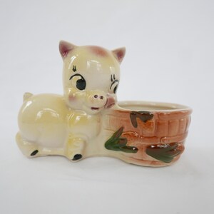 May include: A vintage ceramic pig-shaped planter. The pig is light yellow with a reddish-brown brick-effect planter. The pig has black eyes and a pink snout. A decorative item for the home.