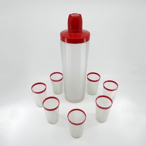May include: A set of seven clear glass cocktail glasses with red rims, including a tall shaker with a red lid. The glasses have a ribbed texture.