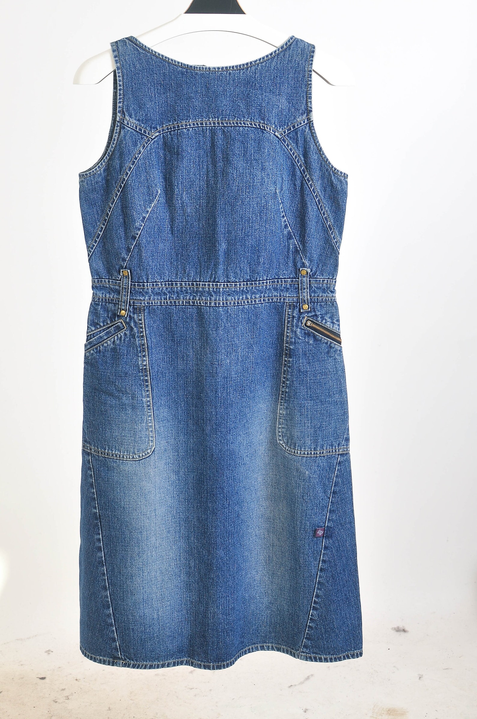 Vintage 00s denim dress in mid-blue. Sleeveless mini dress with a round neck and wide straps, cinched waist, belt loops, and 2 side pockets with a zip detail. Back zip.