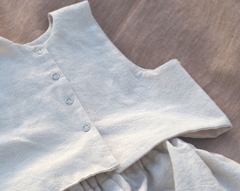 May include: A white sleeveless top with a gathered skirt. The top has a round neckline and a button fastening. The skirt is gathered at the waist and has a flowing silhouette.
