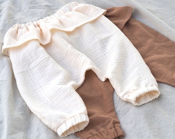May include: A pair of off-white cotton pants with a ruffle detail at the waist, and a pair of brown cotton pants.