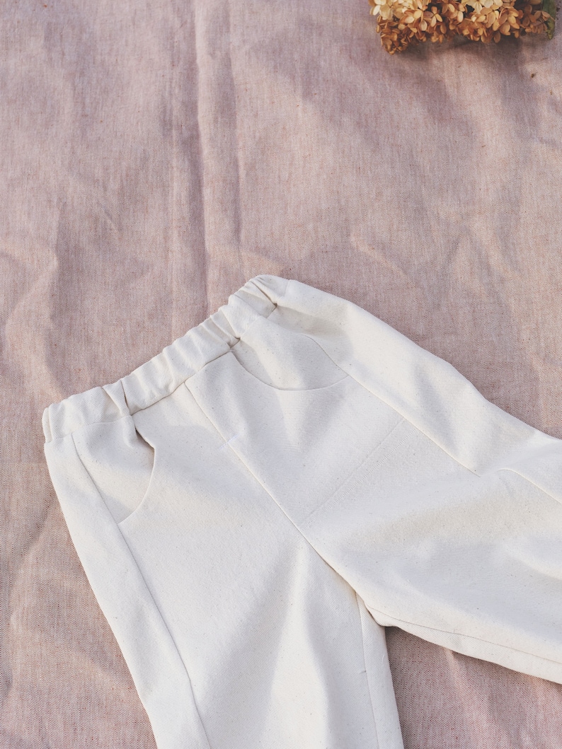 Op de afbeelding: Witte katoenen broek met een ontspannen pasvorm en een trekkoord in de taille. De broek heeft twee grote zakken aan de voorkant.