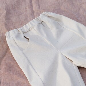Op de afbeelding: Een off-white broek met een trekkoord in de taille en twee zakken. De broek is gemaakt van een zachte, lichte stof.
