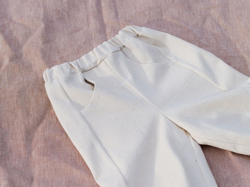 Op de afbeelding: Een off-white broek met een trekkoord in de taille en twee zakken. De broek is gemaakt van een zachte, lichte stof.