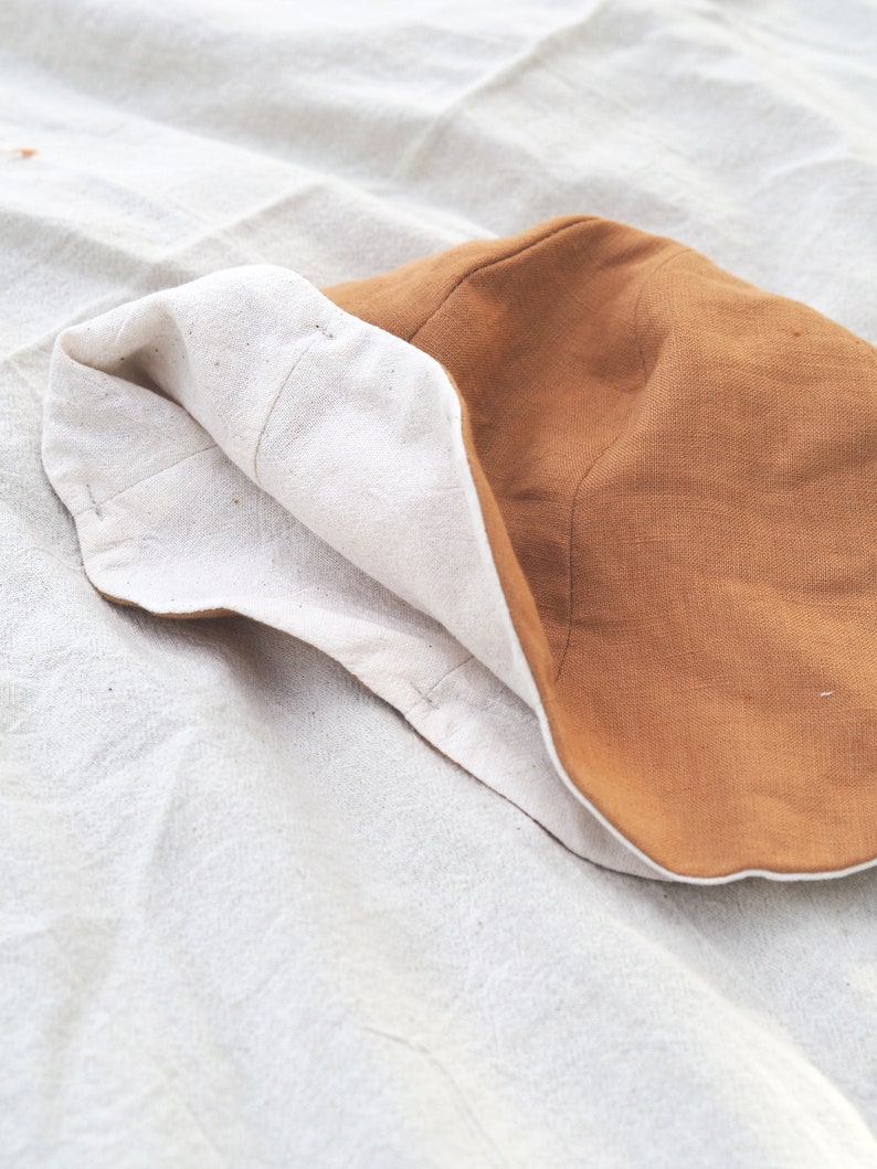 May include: A brown and white bucket hat made of fabric. The hat is folded in half and the brown side is facing up.