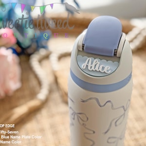 May include: A white water bottle featuring a pastel blue flip-top lid and a scalloped name plate with the name Alice in white script. The bottle body is decorated with a light blue ribbon pattern. Text on the image reads: SCALLOP EDGE, Font Fifty-Seven, Pastel Blue Name Plate Color, White Name Color.
