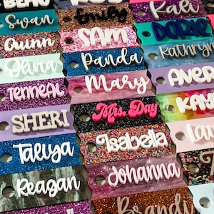May include: A collection of colorful, glittery name tags with various names written in white, pink, and blue lettering. The names include "Swan", "Quinn", "Dana", "Tenneal", "Sheri", "Taliya", "Reagan", "Sam", "Panda", "Mary", "Mrs. Day", "Isabella", "Johanna", "Kali", "Dorrie", "Kathryn", "Avery", "Kaylee", "Lauren", "Ash", and "Aoi".