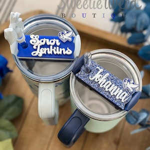 May include: Two tumblers with handles and clear lids, each featuring a custom name plate. The left plate is matte royal blue with white text reading Soror Jenkins. The right plate is glittery royal blue with white text reading Johanna.