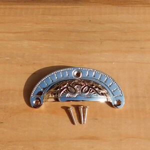 May include: A silver-toned, ornate, half-round cabinet pull with a decorative floral design. The pull comes with two screws.