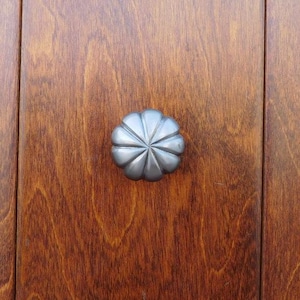 May include: A silver, decorative door knob with a starburst design. The knob is mounted on a wooden door.