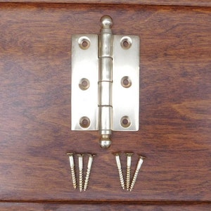 Peut inclure: Une charnière de porte argentée avec un bouton arrondi en haut et en bas. La charnière est accompagnée de huit petites vis.