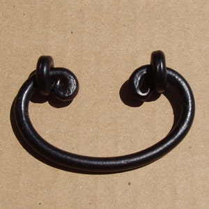 May include: Black metal drawer pull with a knotted design. The pull is shaped like a rounded rectangle with a slight curve in the middle.