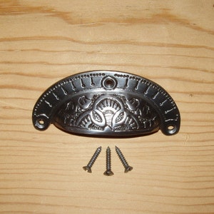 Puede incluir: Tirador de cajón de metal negro con un diseño adornado y tres tornillos.