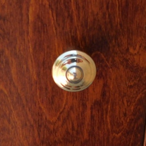 Puede incluir: Un pomo de puerta redondo de plata con un anillo central elevado.