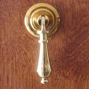 May include: A gold-toned cabinet pull with a round base and a long, slender handle.