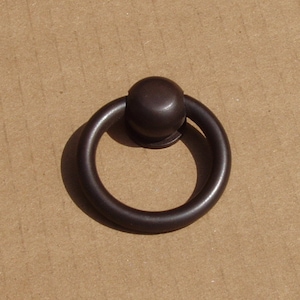 Könnte beinhalten: Ein schwarzer Metallring-Zuggriff mit einem runden Knopf. Der Griff ist für Schränke, Schubladen oder Türen konzipiert.