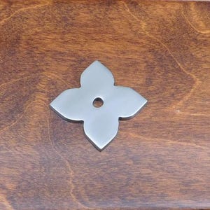 Peut inclure: Un élément de quincaillerie décoratif en métal argenté en forme d'étoile à quatre branches avec un trou au centre.