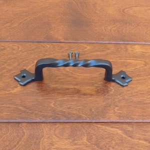 Może przedstawiać: Czarny metalowy klamka do drzwi z zakręconym wzorem. Klamka ma kwadratowy kształt na każdym końcu.