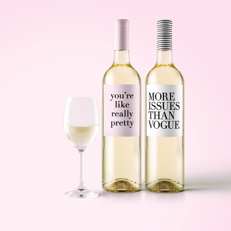 May include: Two wine bottles with humorous labels and a wine glass filled with white wine. One bottle has a pink label with the text "you're like really pretty." The other bottle has a white label with the text "MORE ISSUES THAN VOGUE."