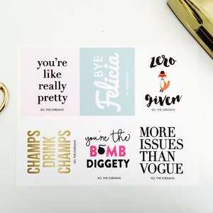 May include: A sheet of stickers with various phrases in black and gold, including "you're like really pretty" and "zero given." A gold pair of scissors and a gold stapler are in the background.