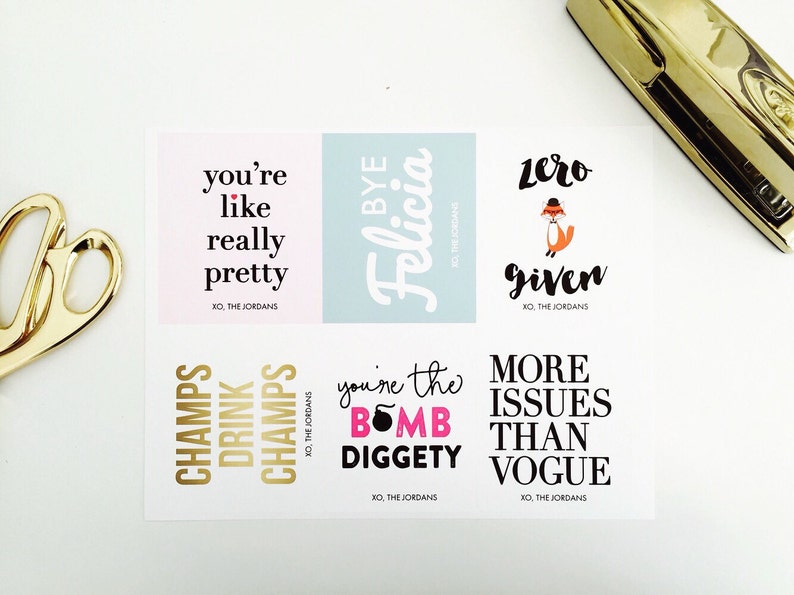 May include: A sheet of stickers with various phrases in black and gold, including "you're like really pretty" and "zero given." A gold pair of scissors and a gold stapler are in the background.