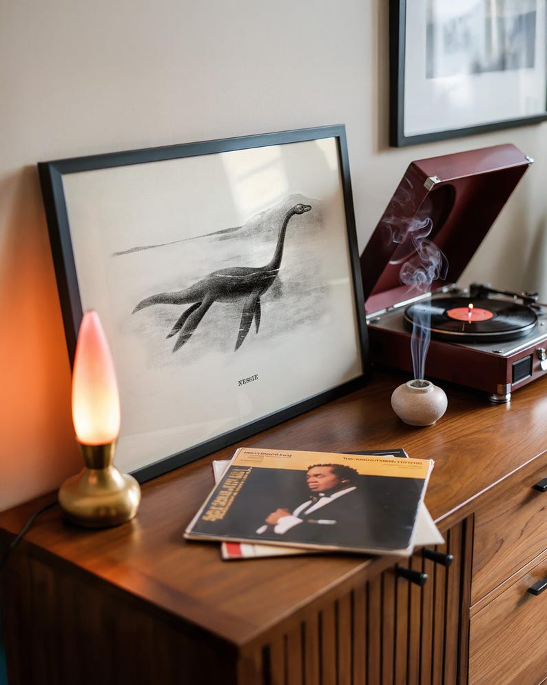 Pode incluir: Uma ilustra&ccedil;&atilde;o em preto e branco emoldurada do Monstro do Lago Ness, rotulada como "Nessie", est&aacute; em um arm&aacute;rio de madeira. Um toca-discos vintage com a parte superior vermelha est&aacute; aberto, tocando um disco. Uma pequena l&acirc;mpada com base dourada e abajur rosa e branco est&aacute; acesa.