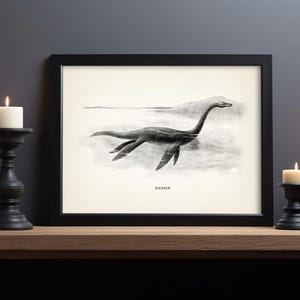 Pode incluir: Impress&atilde;o emoldurada em preto com uma ilustra&ccedil;&atilde;o vintage do Monstro do Lago Ness, ou Nessie, em um lago. A obra de arte &eacute; em preto e branco, com a palavra "NESSIE" impressa abaixo da imagem. A impress&atilde;o &eacute; exibida em uma superf&iacute;cie de madeira.
