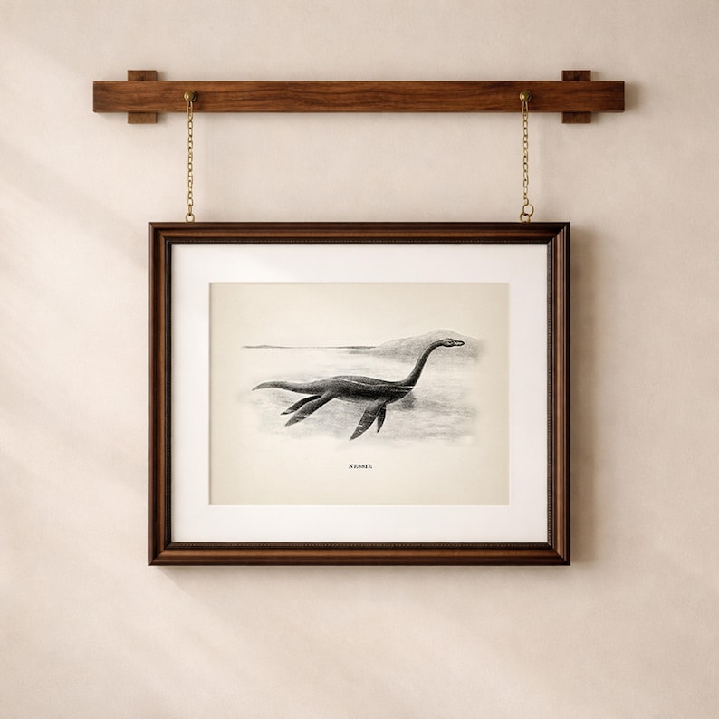 Pode incluir: Ilustra&ccedil;&atilde;o em preto e branco emoldurada do Monstro do Lago Ness, ou Nessie, nadando em um lago. A obra de arte est&aacute; em uma moldura de madeira marrom escura, pendurada em uma barra de madeira com correntes douradas.