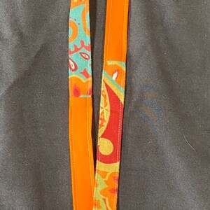 May include: A bright orange lanyard with a colorful paisley pattern. The lanyard has a silver swivel clip.