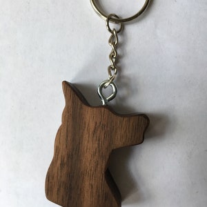 May include: A wooden dog head keychain with a silver chain and ring. The keychain is made of dark brown wood with a natural grain pattern.