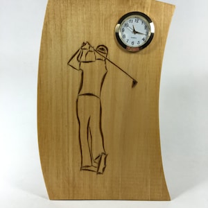 May include: A wooden clock with a golfer silhouette and a round clock face with black hands and gold trim. The clock face reads "QUARTZ" and has numbers 1 through 12.