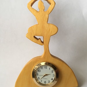 May include: A wooden clock shaped like a ballerina with a gold-colored face and black hands. The clock face reads "QUARTZ" and has numbers 1 through 12.