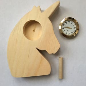 May include: Unfinished wooden unicorn head with a small round clock face in the center. The clock face has gold hands and a gold rim. The unicorn head is a blank canvas for painting or decorating.