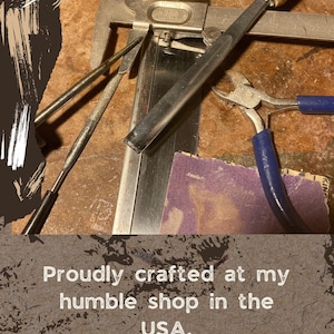 May include: Close-up of various metal tools, including a caliper, files, and a chisel with a wooden handle. The tools are arranged on a textured surface. Text reads: "Proudly crafted at my humble shop in the USA."