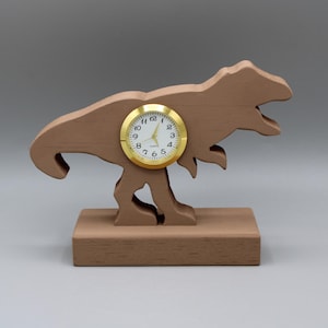 May include: A wooden dinosaur clock with a gold-colored face and black hands. The clock is standing on a wooden base.