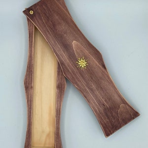 May include: A wooden box with a hinged lid. The box is stained a dark brown color and has a gold sun design on the lid. The inside of the box is a light wood color.