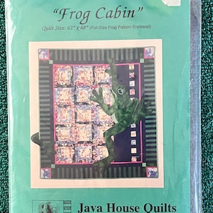 May include: A quilt pattern titled "Frog Cabin" is displayed in a clear plastic package. The quilt design features a green frog on a patterned background. The package includes the text "Quilt Size: 62" x 68"" and the Java House Quilts logo.