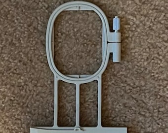 Può includere: Un telaio da ricamo in plastica bianca con una pinza a cerniera. Il telaio è progettato per mantenere il tessuto teso per i progetti di ricamo.