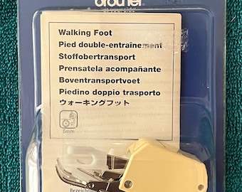 May include: A Brother walking foot sewing machine attachment in a blue and clear plastic package. The package includes a cream-colored foot and a label with the text "Walking Foot" in multiple languages. The package is on a teal surface.