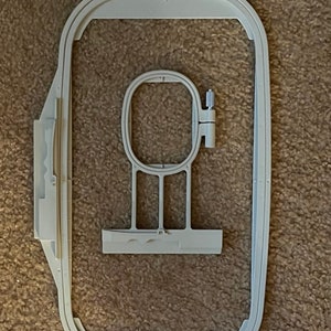 Puede incluir: Un aro de bordado de plástico blanco con un aro interior más pequeño. El aro está diseñado para usarse con una máquina de coser.
