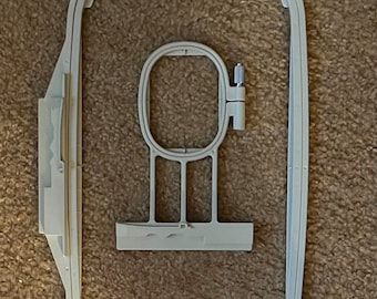 Può includere: Un cerchio da ricamo in plastica bianca con un cerchio interno più piccolo. Il cerchio è progettato per essere utilizzato con una macchina da cucire.