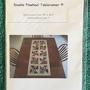 May include: A package for a Double Pinwheel Tablerunner. The approximate size is 44" x 18.5" with a finished block size of 7". The image shows a completed tablerunner with a pinwheel design in shades of red, green, and beige.