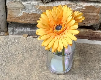 Mandy: 5 1/2 inches Golden daisies in a small opal cylinder glass vase with hard water inside. (Silk flowers)