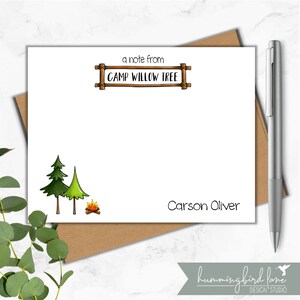 May include: A white card with a handwritten note from Camp Willow Tree. The card features a drawing of two green pine trees and a campfire. The name Carson Oliver is written at the bottom of the card.